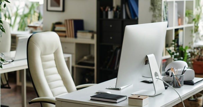 A simple home office setup with a computer monitor and supplies on a grey desk, and a white leather armchair in front